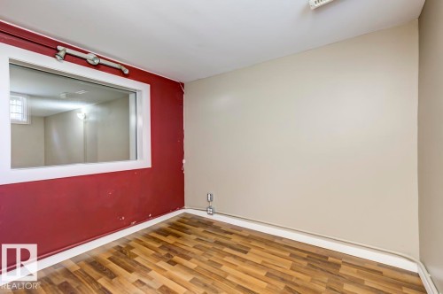 Room featuring wood-finish flooring, a large interior window with white trim, and a combination of red and neutral-toned wall finishes - 9602 90 Street, Edmonton, AB - Indoor Photo Showing Other Room