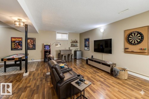Spacious entertainment room featuring wood-finish flooring, a built-in wet bar with shelving, a wall-mounted television, and a recessed window - 9602 90 Street, Edmonton, AB - Indoor