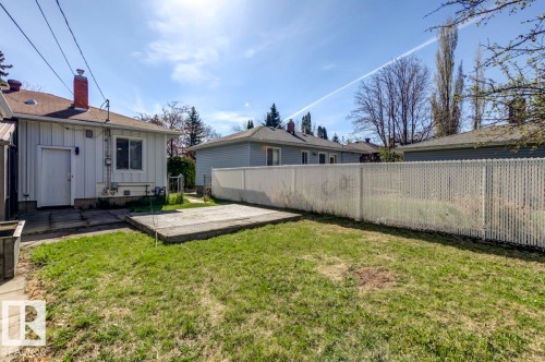 Spacious green lawn with a concrete patio, privacy fencing, and a white exterior building featuring a red brick chimney - 9602 90 Street, Edmonton, AB - Outdoor