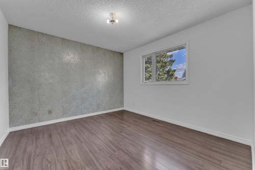 Room featuring wood-finish flooring, a textured accent wall, white baseboards, and a window with white trim - 3520 19 Avenue, Edmonton, AB - Indoor Photo Showing Other Room