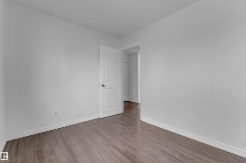 Spacious room featuring light gray walls, wood-finish flooring, white baseboards, and a white interior door with a silver-tone knob - 3520 19 Avenue, Edmonton, AB - Indoor Photo Showing Other Room