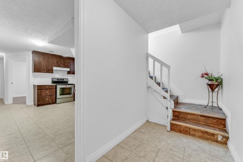 Tiled flooring extending from the entry area into a kitchen space featuring dark wood cabinetry, a stainless steel range, and a white subway tile backsplash - 3520 19 Avenue, Edmonton, AB - Indoor Photo Showing Other Room