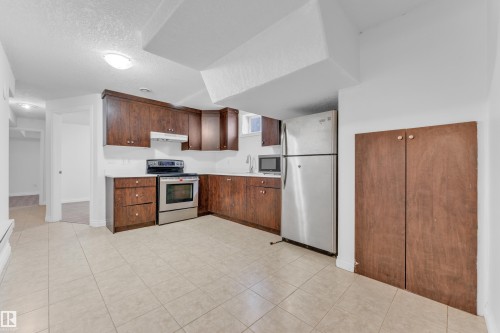 Kitchen featuring dark wood cabinetry, stainless steel appliances, light-toned countertops, and ceramic tile flooring - 3520 19 Avenue, Edmonton, AB - Indoor Photo Showing Kitchen