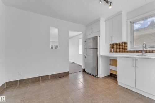 Bright kitchen area featuring white cabinetry, a stainless steel refrigerator, white countertops, a mosaic tile backsplash, and a window above the sink - 3520 19 Avenue, Edmonton, AB - Indoor Photo Showing Kitchen