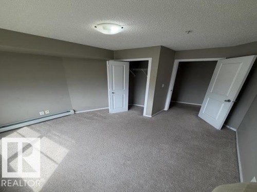 Spacious room featuring neutral carpeting, light gray wall tones, baseboard heating, a flush-mount ceiling light, and two white panel doors - 321 107 Watt Common, Edmonton, AB - Indoor Photo Showing Other Room