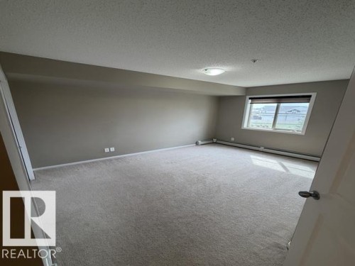 Expansive carpeted room with neutral paint, featuring a large window with blinds and baseboard heating - 321 107 Watt Common, Edmonton, AB - Indoor Photo Showing Other Room