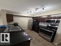 Kitchen featuring dark wood-finish cabinetry, black countertops, and stainless steel appliances - 321 107 Watt Common, Edmonton, AB  - Indoor Photo Showing Kitchen With Double Sink 