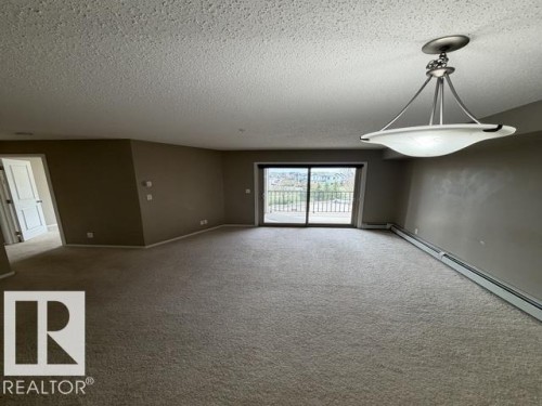 Spacious living area featuring neutral carpeting, a modern ceiling light fixture, and a sliding glass door providing outdoor access - 321 107 Watt Common, Edmonton, AB - Indoor Photo Showing Other Room