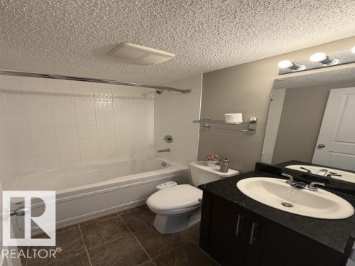 Full bathroom with a white tub and shower surround, dark brown floor tiles, and a dark wood-finish vanity with a light-colored countertop - 321 107 Watt Common, Edmonton, AB - Indoor Photo Showing Bathroom