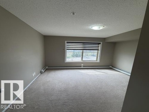 Spacious room featuring neutral carpeting, light-toned walls, and a large window with horizontal blinds - 321 107 Watt Common, Edmonton, AB - Indoor Photo Showing Other Room