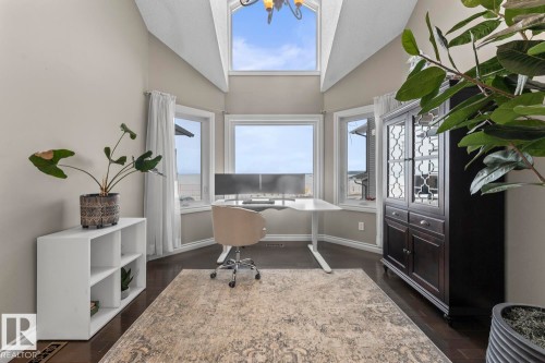 This bright room features a vaulted ceiling with an overhead light fixture, large windows offering outdoor views, and dark wood flooring - 515 Lakeshore Drive, Cold Lake, AB - Indoor Photo Showing Office