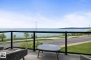 The property features a balcony with a glass railing, providing views of the water, a paved road, and a landscaped green area with trees - 515 Lakeshore Drive, Cold Lake, AB  - Outdoor With Body Of Water With View 