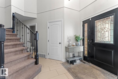Welcoming entryway featuring a double front door with decorative glass inserts, light-toned tile flooring, and a carpeted staircase with an ornamental metal railing - 515 Lakeshore Drive, Cold Lake, AB - Indoor Photo Showing Other Room