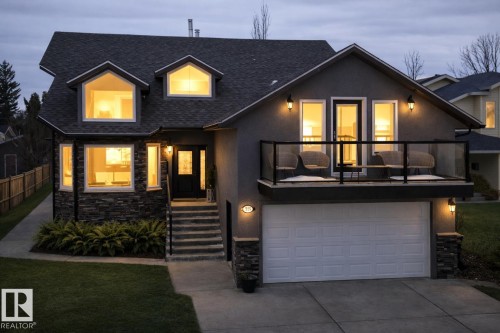 This property features a two-car garage with a concrete driveway, a stone facade, and a balcony with a glass railing - 515 Lakeshore Drive, Cold Lake, AB - Outdoor