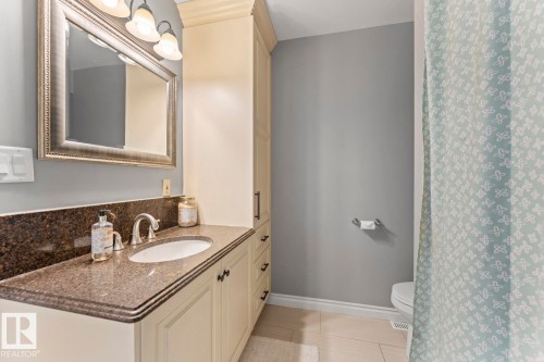 This bathroom features a vanity with a dark granite countertop and a built-in sink, complemented by a large framed mirror and a light fixture with three sconces - 515 Lakeshore Drive, Cold Lake, AB - Indoor Photo Showing Bathroom