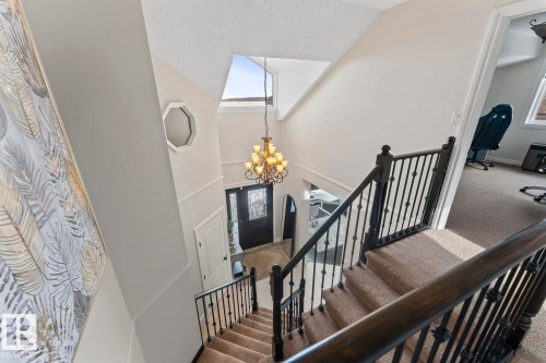 Inviting staircase with carpeted steps and dark wood and metal railings, leading to a front entry with a decorative dark wood door and a chandelier overhead - 515 Lakeshore Drive, Cold Lake, AB - Indoor Photo Showing Other Room