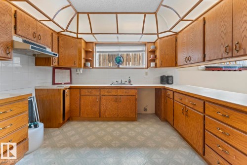 Kitchen with extensive wood cabinetry, a sink below a window, and a range hood above a tiled backsplash - 515 Lakeshore Drive, Cold Lake, AB - Indoor Photo Showing Kitchen
