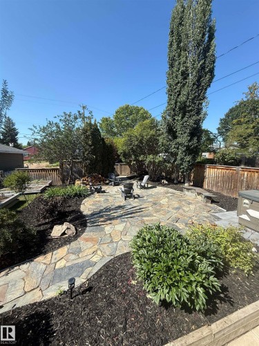 The property features a stone patio with a fire pit, surrounded by landscaped garden beds and a wooden fence - 515 Lakeshore Drive, Cold Lake, AB - Outdoor