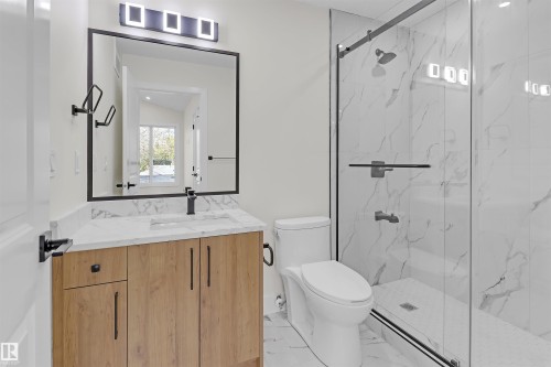 Modern bathroom featuring a wood-finish vanity with a white countertop and rectangular sink, a frameless shower with a glass door, and large-format white tile flooring - 7936 91 Avenue, Edmonton, AB - Indoor Photo Showing Bathroom
