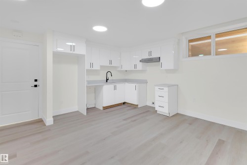 Modern kitchen area featuring white cabinetry, a black gooseneck faucet, light grey countertops, and wood-finish flooring - 7936 91 Avenue, Edmonton, AB - Indoor Photo Showing Kitchen