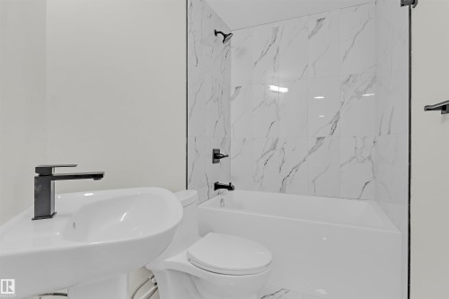 Bathroom featuring a white pedestal sink, matte black faucet, and a white bathtub with white-veined tile surround - 7936 91 Avenue, Edmonton, AB - Indoor Photo Showing Bathroom
