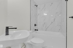 Bathroom featuring a white pedestal sink, matte black faucet, and a white bathtub with white-veined tile surround - 