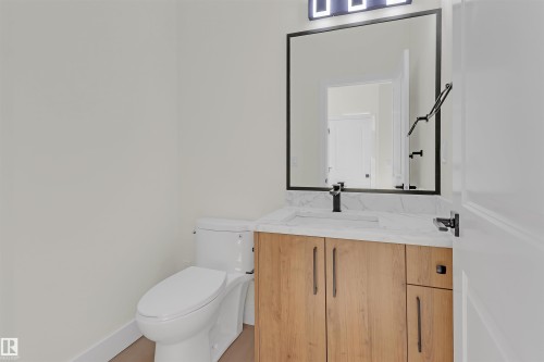 Bathroom featuring a wood-finish vanity with a rectangular sink, a light-toned countertop, and matte black fixtures - 7936 91 Avenue, Edmonton, AB - Indoor Photo Showing Bathroom