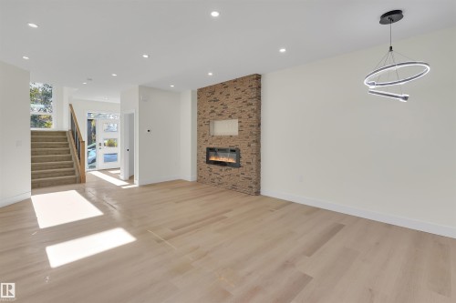 Spacious living area featuring light wood-finish flooring and a contemporary fireplace with a stacked stone facade - 7936 91 Avenue, Edmonton, AB - Indoor With Fireplace