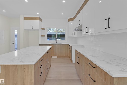 Modern kitchen featuring a large central island with a quartz countertop, wood-finish cabinetry, white upper cabinets with matte black hardware, a white subway tile backsplash, and recessed lighting - 7936 91 Avenue, Edmonton, AB - Indoor Photo Showing Kitchen With Upgraded Kitchen