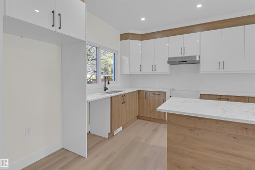 Contemporary kitchen featuring two-tone cabinetry with white upper cabinets and wood-finish lower cabinets, stone-finish countertops, and a central island - 7936 91 Avenue, Edmonton, AB - Indoor Photo Showing Kitchen