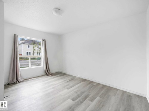 Light-filled room featuring a large window, contemporary wood-finish flooring, white walls, and a ceiling-mounted light fixture - 4322 53 Street, Wetaskiwin, AB - Indoor Photo Showing Other Room
