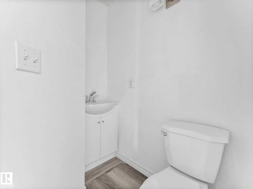 Compact powder room featuring a corner vanity with a white cabinet and integrated sink, chrome faucet, and wood-finish flooring - 4322 53 Street, Wetaskiwin, AB - Indoor Photo Showing Bathroom