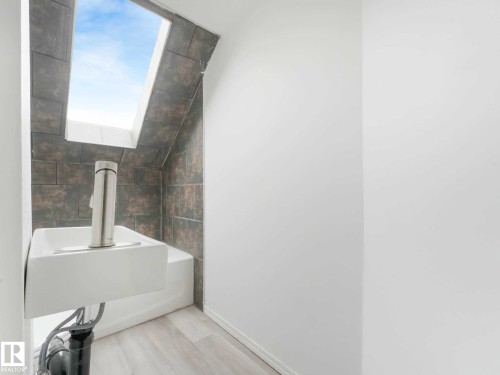 Compact bathroom featuring a rectangular skylight, wall-mounted sink, and modern chrome faucet - 4322 53 Street, Wetaskiwin, AB - Indoor Photo Showing Bathroom