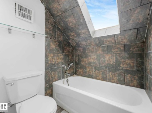 Bathroom with a clean white bathtub and toilet, complemented by textured grey wall tiling - 4322 53 Street, Wetaskiwin, AB - Indoor Photo Showing Bathroom