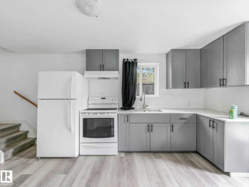 Contemporary kitchen featuring light gray shaker-style cabinetry with dark hardware, white countertops, and a stainless steel sink with a gooseneck faucet - 4322 53 Street, Wetaskiwin, AB - Indoor Photo Showing Kitchen