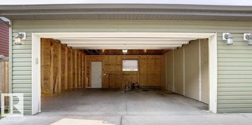 Spacious garage with an open overhead door, featuring concrete flooring, interior framing, and a utility door - 225 51A Street, Edmonton, AB 