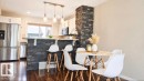 Kitchen featuring a stone-clad island with seating, stainless steel appliances, white cabinetry, and wood-finish flooring - 225 51A Street, Edmonton, AB 