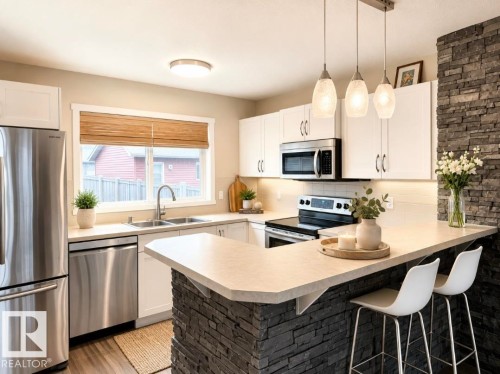 Kitchen featuring white cabinetry, stainless steel appliances, a stone-accented island, pendant lighting, and wood-finish flooring - 225 51A Street, Edmonton, AB 