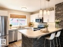 Kitchen featuring white cabinetry, stainless steel appliances, a stone-accented island, pendant lighting, and wood-finish flooring - 225 51A Street, Edmonton, AB 