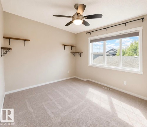 Spacious room featuring neutral carpeting and a ceiling fan with integrated lighting - 225 51A Street, Edmonton, AB 