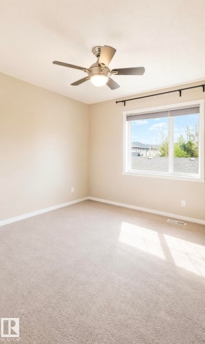 Spacious room featuring neutral carpeting, light-toned walls, and a ceiling fan with integrated lighting - 225 51A Street, Edmonton, AB 