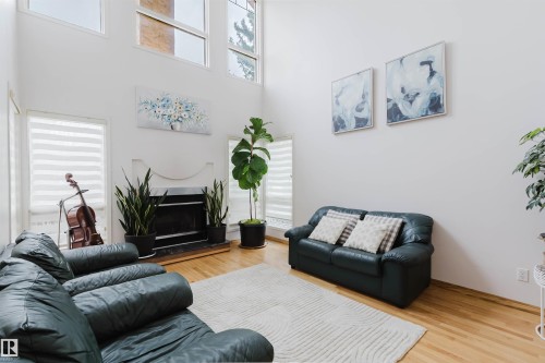 Two-story living area featuring a fireplace with a mantel, light wood-finish flooring, and multiple windows with horizontal blinds - 342 O'Connor Close, Edmonton, AB - Indoor Photo Showing Living Room With Fireplace