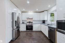Modern kitchen featuring white cabinetry, stainless steel appliances, dark countertop, and recessed lighting - 