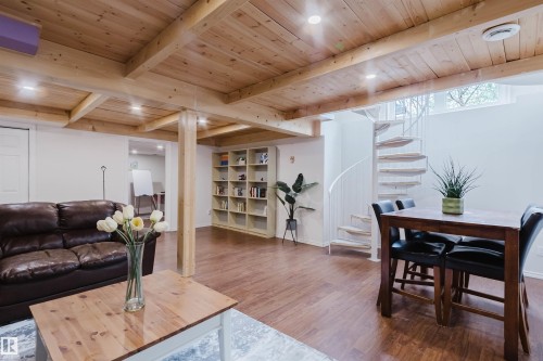 Lower level living area featuring a spiral staircase, wood-finish flooring, exposed wood beam ceiling, and built-in shelving - 342 O'Connor Close, Edmonton, AB - Indoor