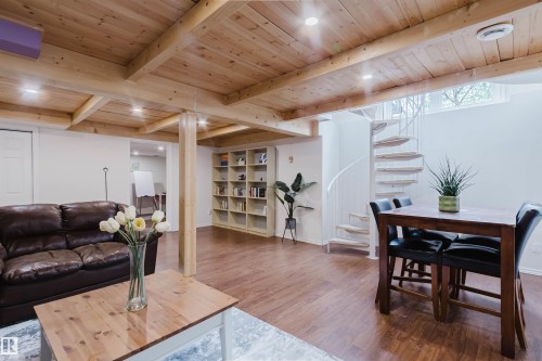 Open-concept interior featuring wood-finish flooring, exposed wooden ceiling beams, recessed lighting, a white spiral staircase, and a built-in shelving unit - 342 O'Connor Close, Edmonton, AB - Indoor