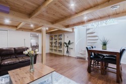 Open-concept interior featuring wood-finish flooring, exposed wooden ceiling beams, recessed lighting, a white spiral staircase, and a built-in shelving unit - 