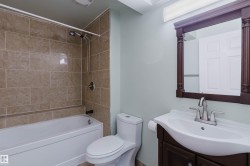 Bathroom featuring a tub and shower combination with full-height tile surround, a dark wood-finish vanity with an integrated sink, a matching framed mirror, and a wall-mounted light fixture - 