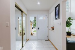 Bright entryway featuring white tiled flooring, a white front door with a decorative half-moon window, an adjacent sidelight window, and a built-in mirrored closet with brass-finish trim - 