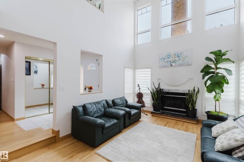 Vaulted ceiling living room featuring a white-painted fireplace with a black hearth, light wood-finish flooring, and multiple upper-level windows - 342 O'Connor Close, Edmonton, AB - Indoor Photo Showing Living Room With Fireplace
