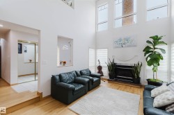 Vaulted ceiling living room featuring a white-painted fireplace with a black hearth, light wood-finish flooring, and multiple upper-level windows - 